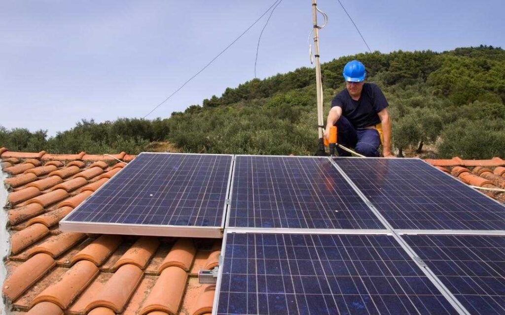 Mężczyzna montuje panele słoneczne na dachu domu jednorodzinnego